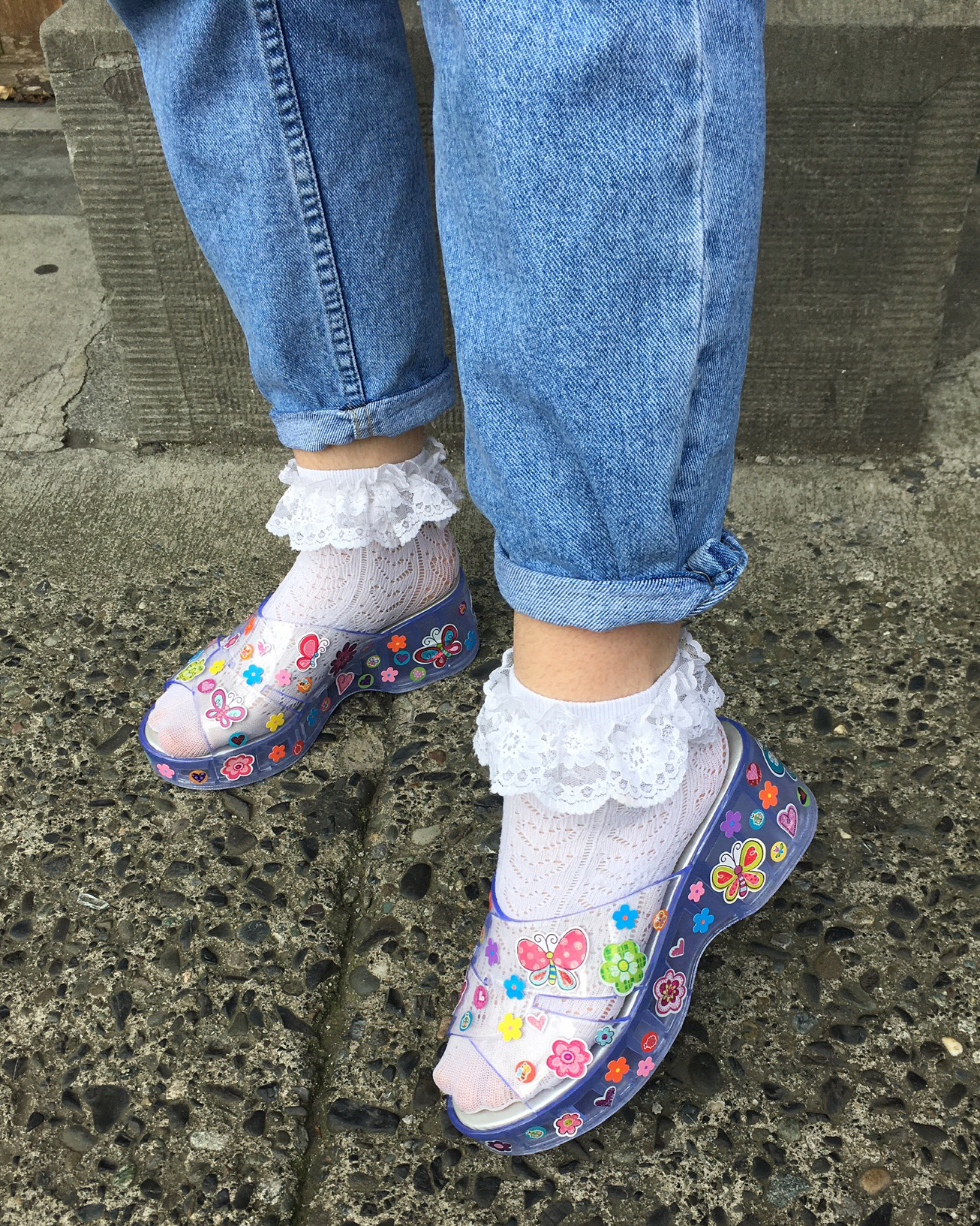 cropped shot of someone wearing transparent plastic shoes covered in stickers, white socks and rolled up jeans