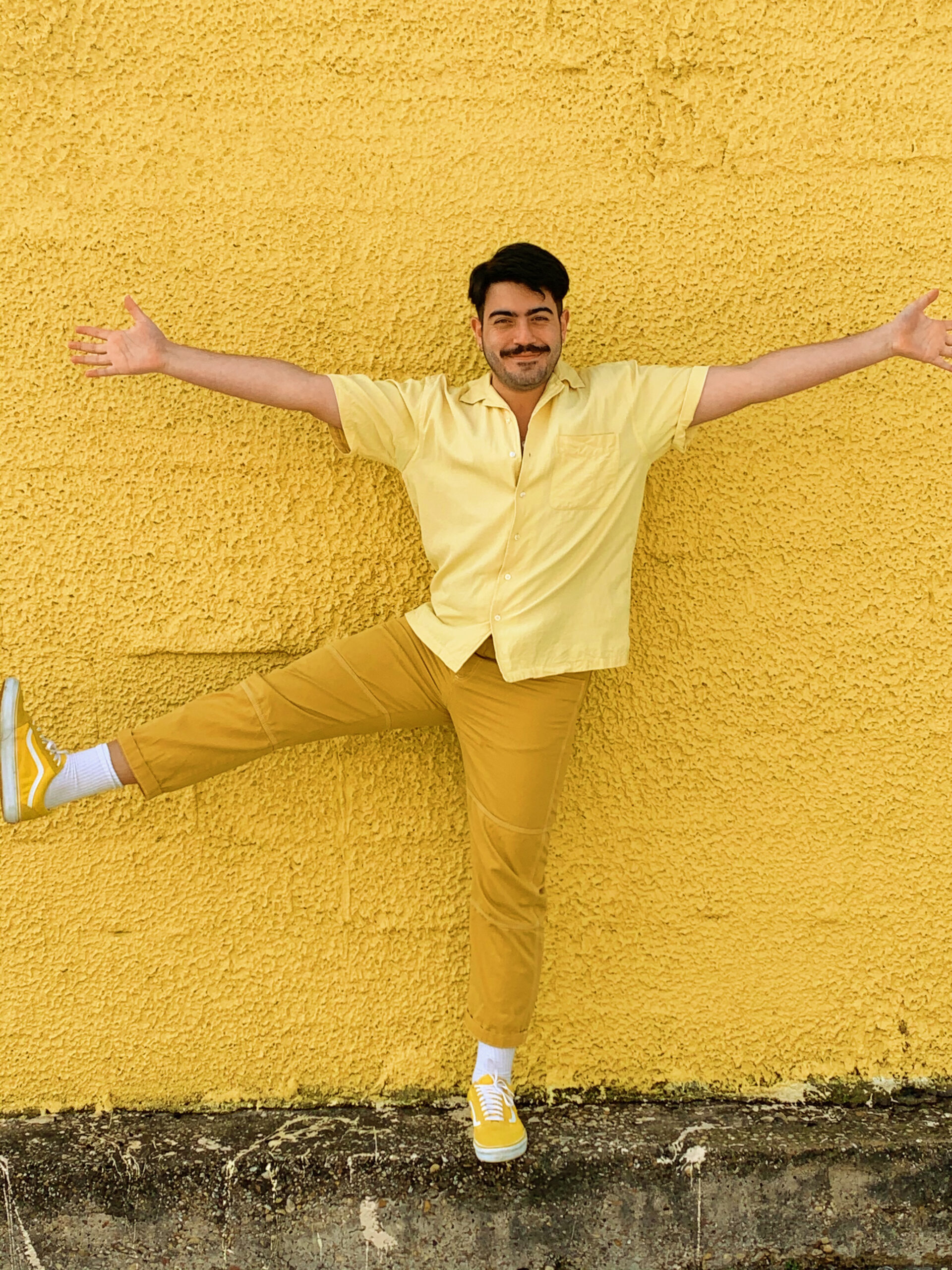 Buffalo Exchange employee posing in front of a yellow wall wearing a head to toe yellow outfit