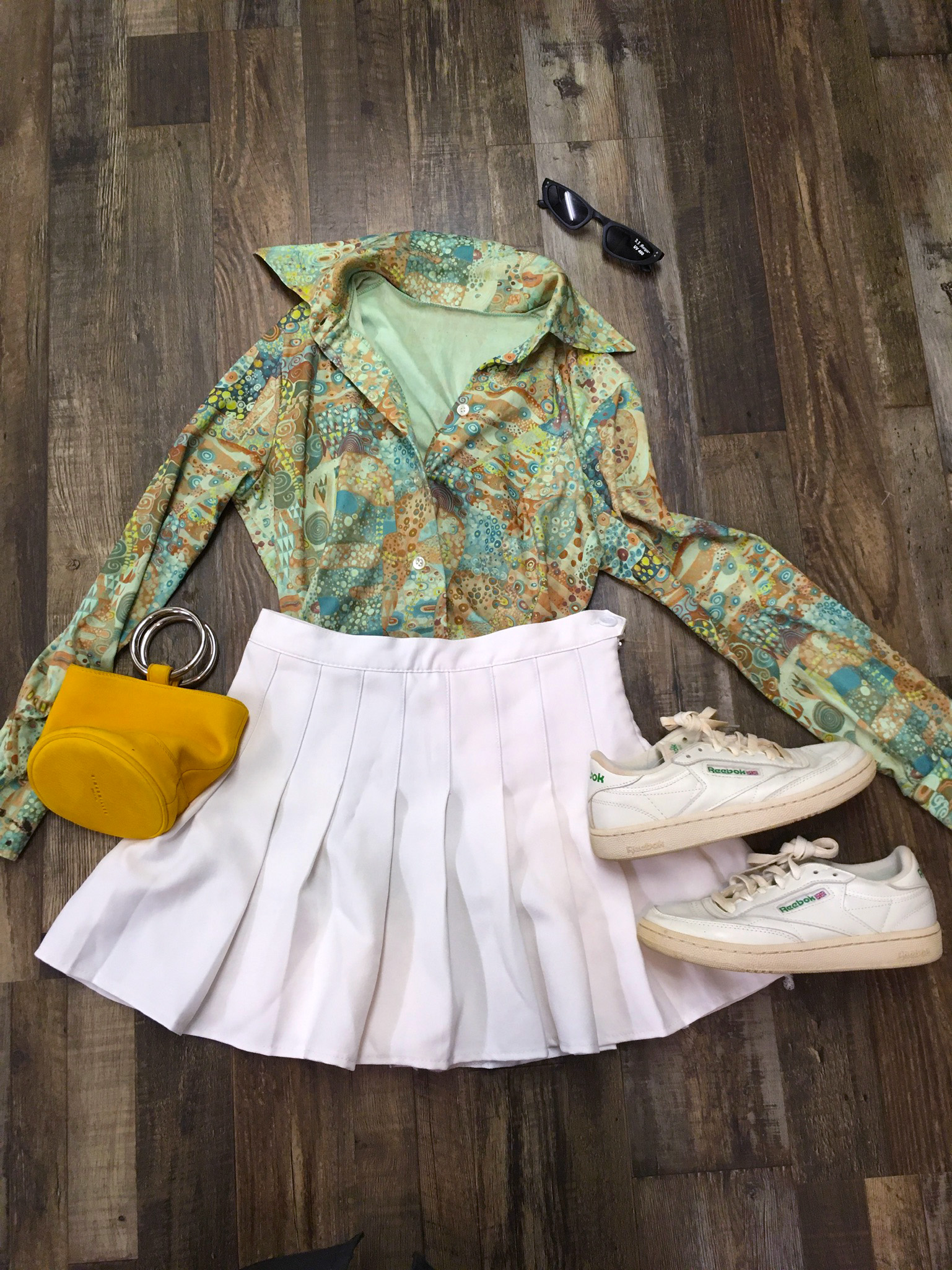 white pleated skirt styled with green paisley blouse, white Reebok sneakers, mustard handbag and tiny black sunglasses