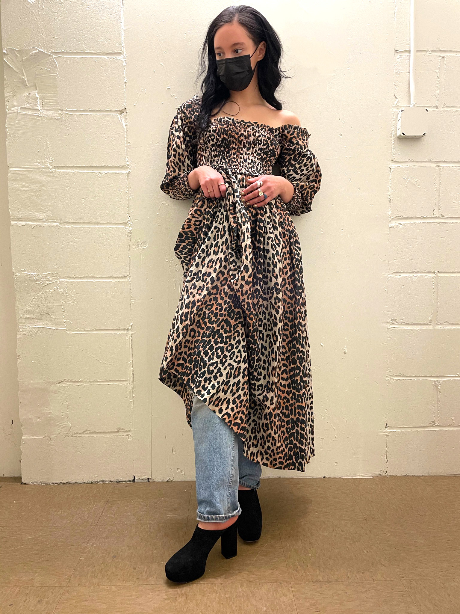 Person standing in front of brick wall wearing leopard print midi dress styled over lightwash jeans and mules