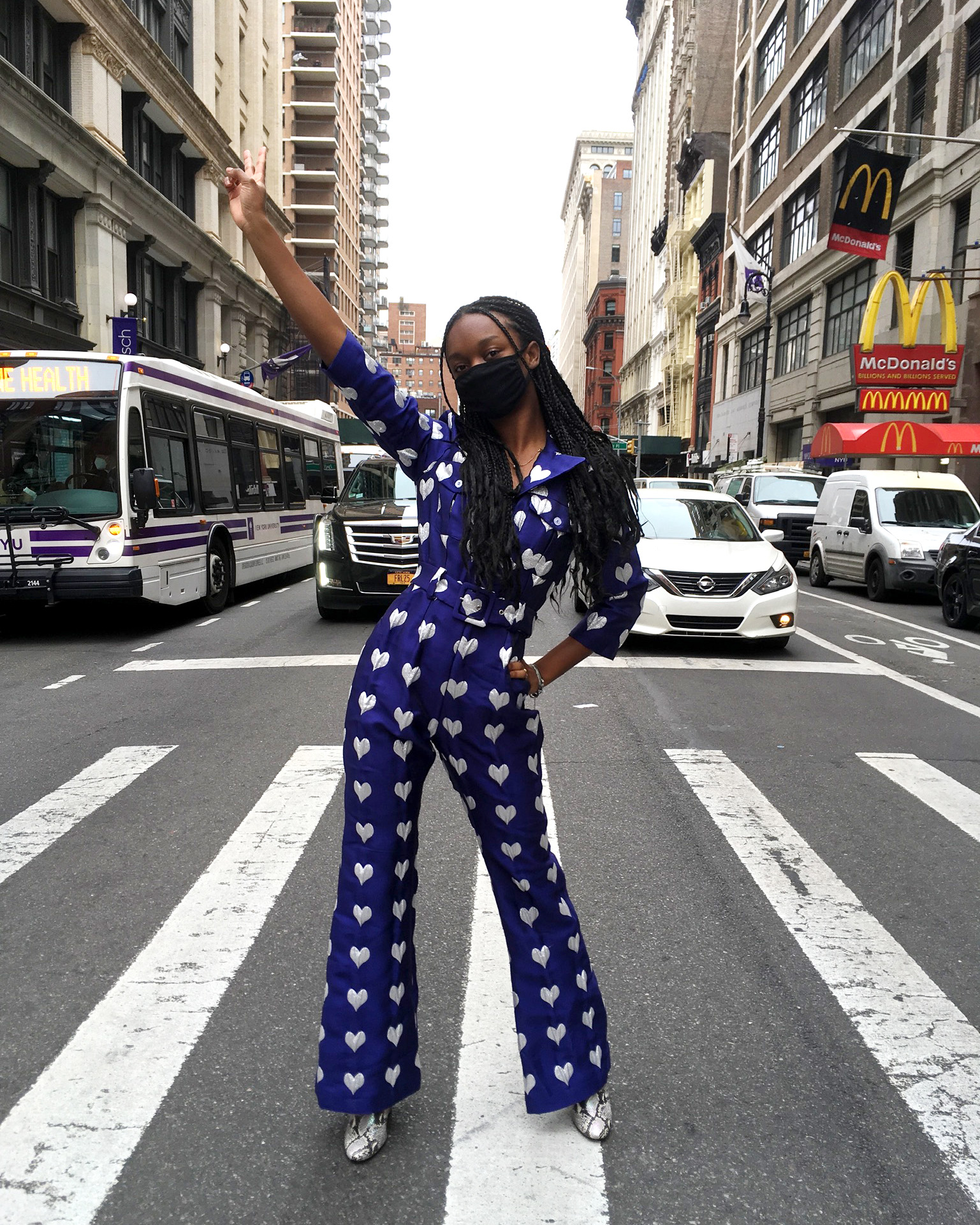 Person posed in middle of sidewalk in front of traffic on New York City street wearing navy blue jumpsuit with silver star embroidery and gray snake print boots