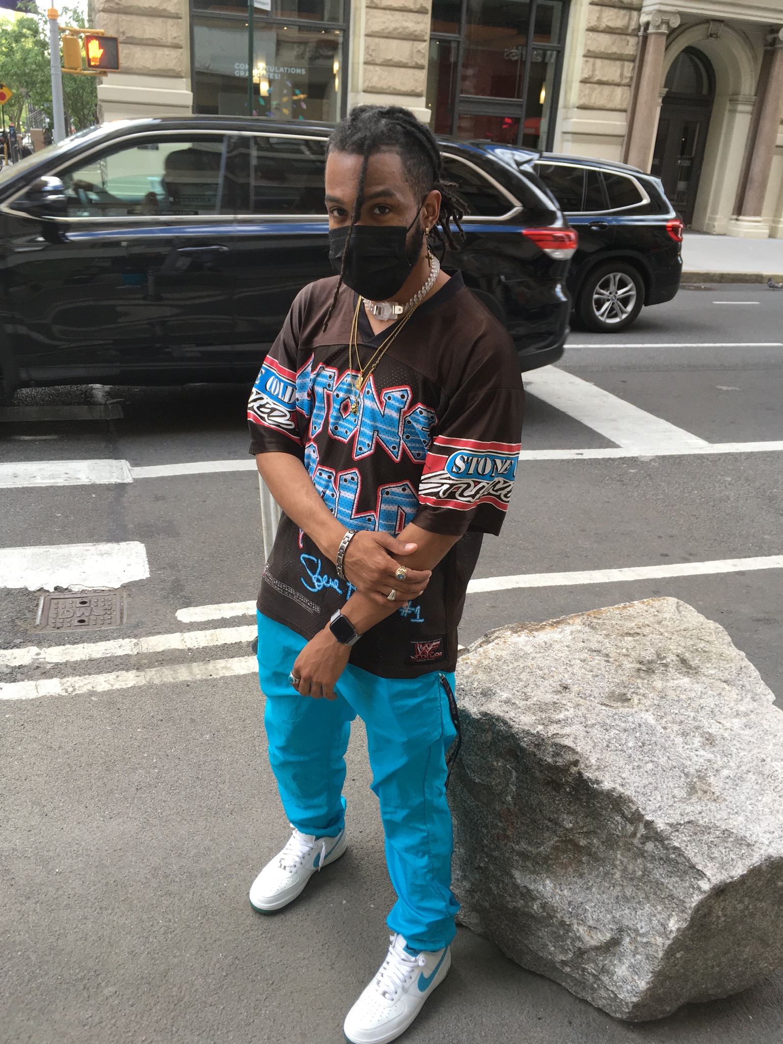 Person stands next to NYC street wearing vintage Stone Cold Steve Austin graphic tee styled with bright blue cargo pants, Nike sneakers and metallic jewelry