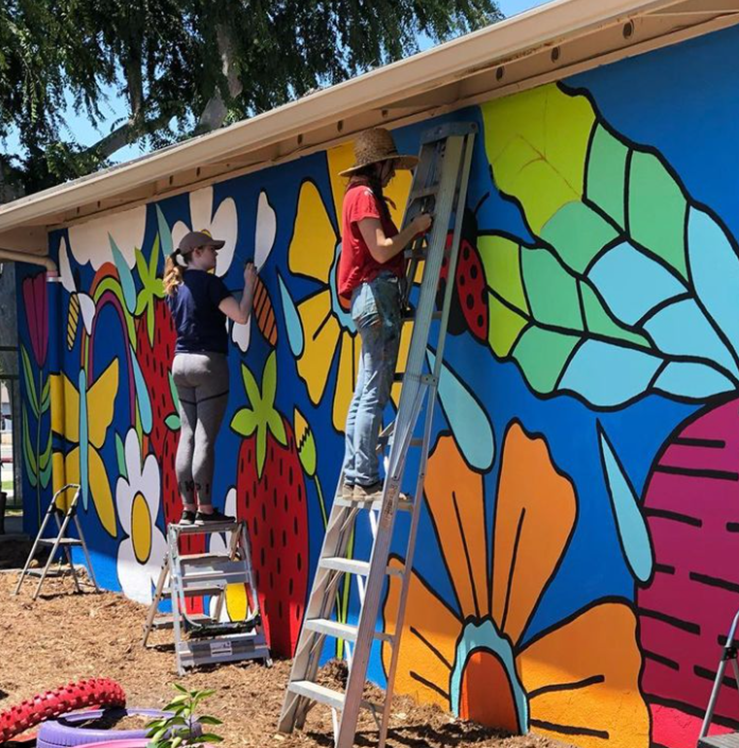 2 people standing on ladders painting colorful floral mural