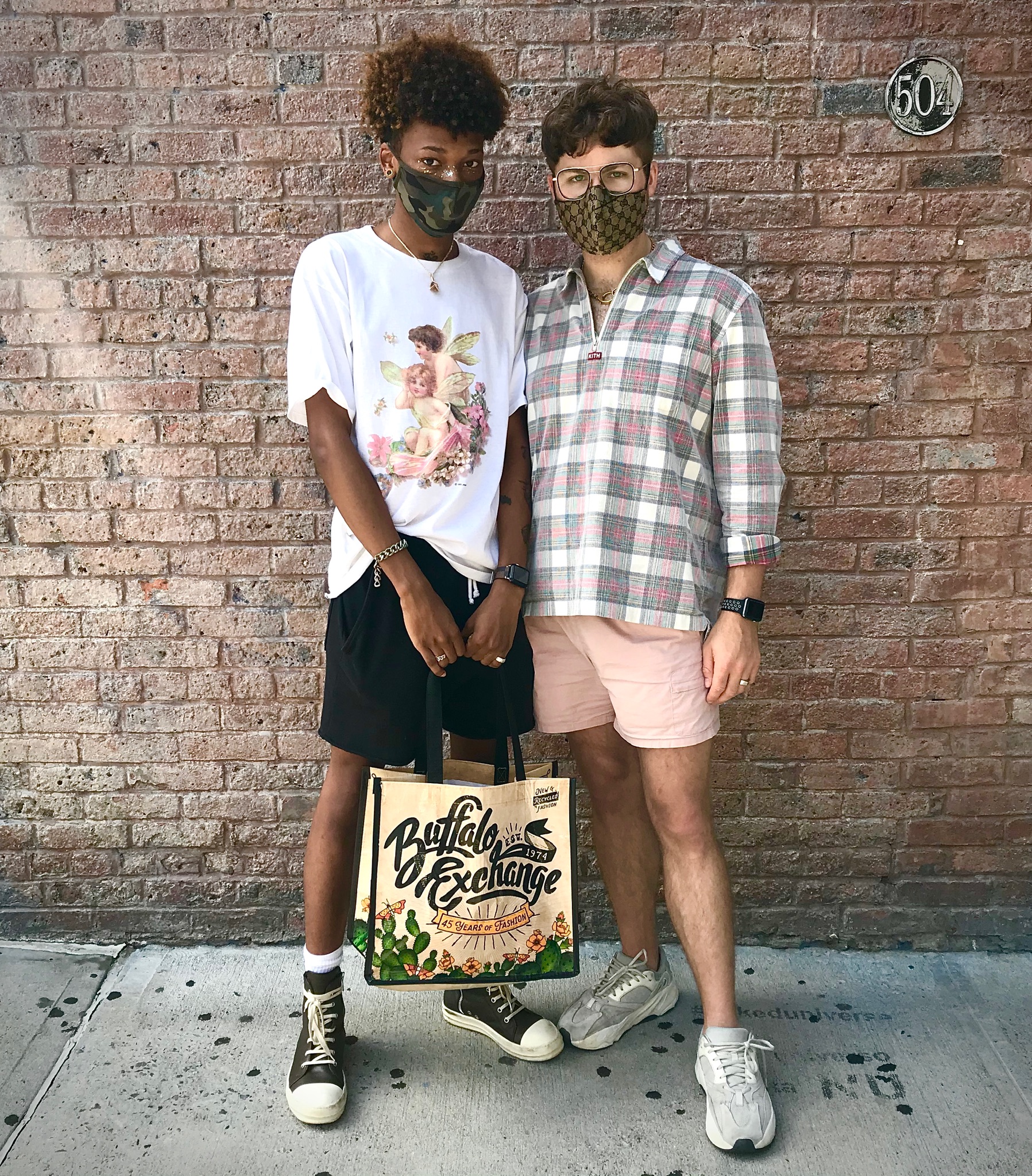 one man wearing a graphic tee and shorts next to another man wearing a plaid shirt and shorts