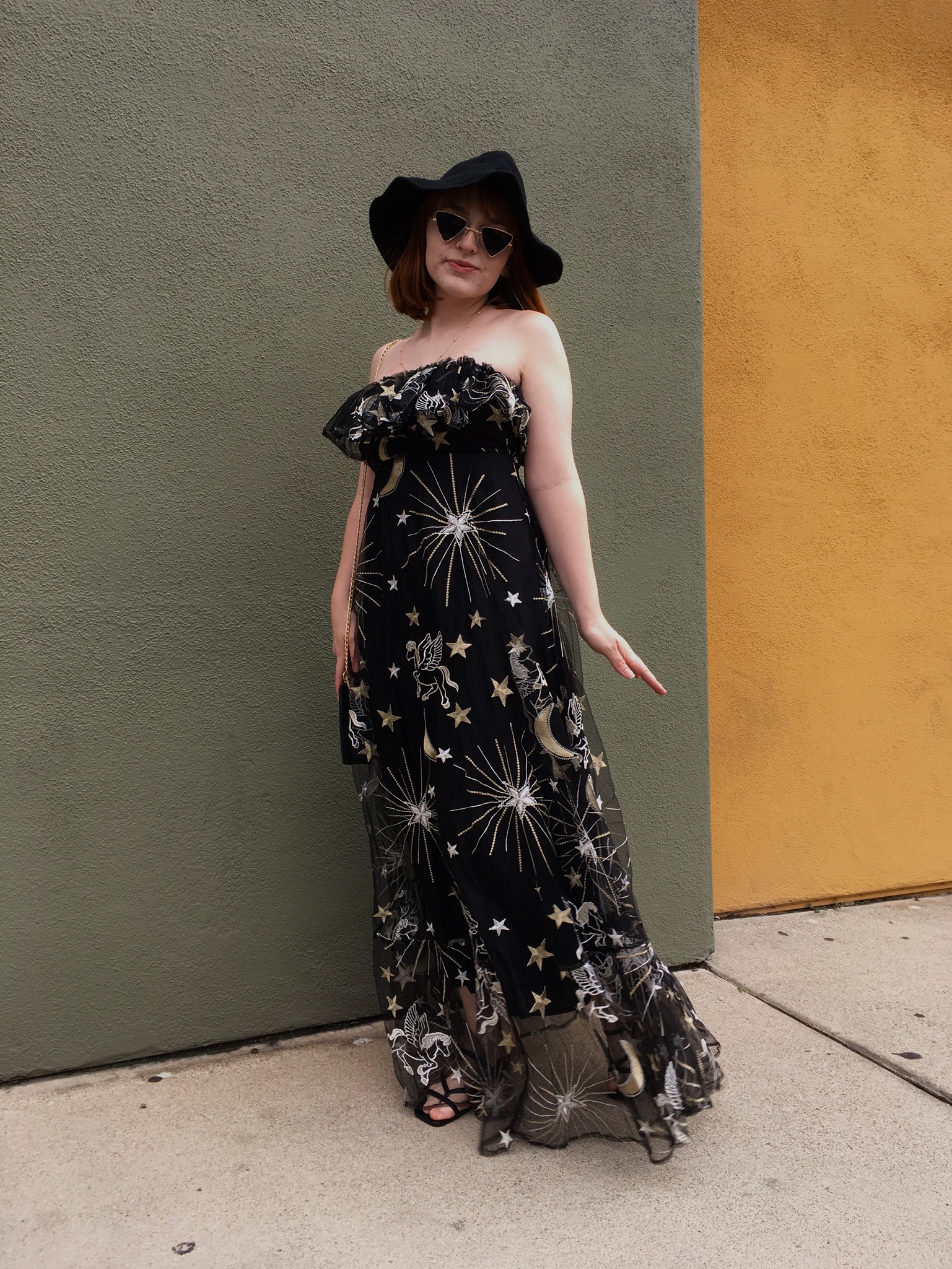 Person standing in front of green wall wearing star pattern dress and black hat