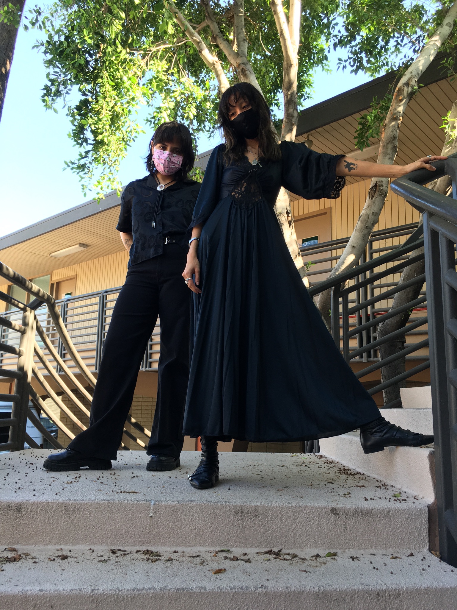 Two people standing at top of steps with tree in background wearing all black outfits
