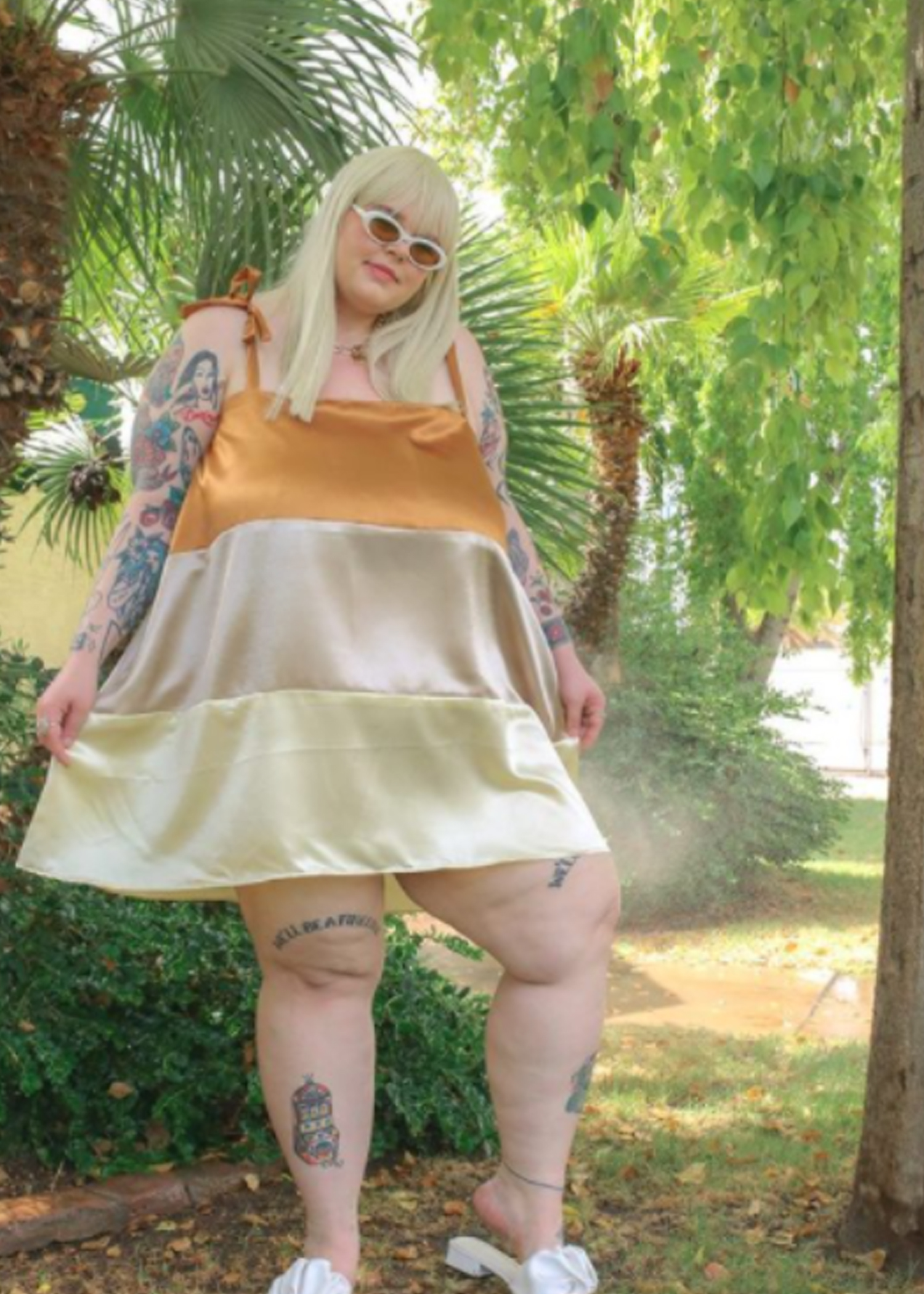 Caelyn wearing a gold and cream mini dress in front of palm trees