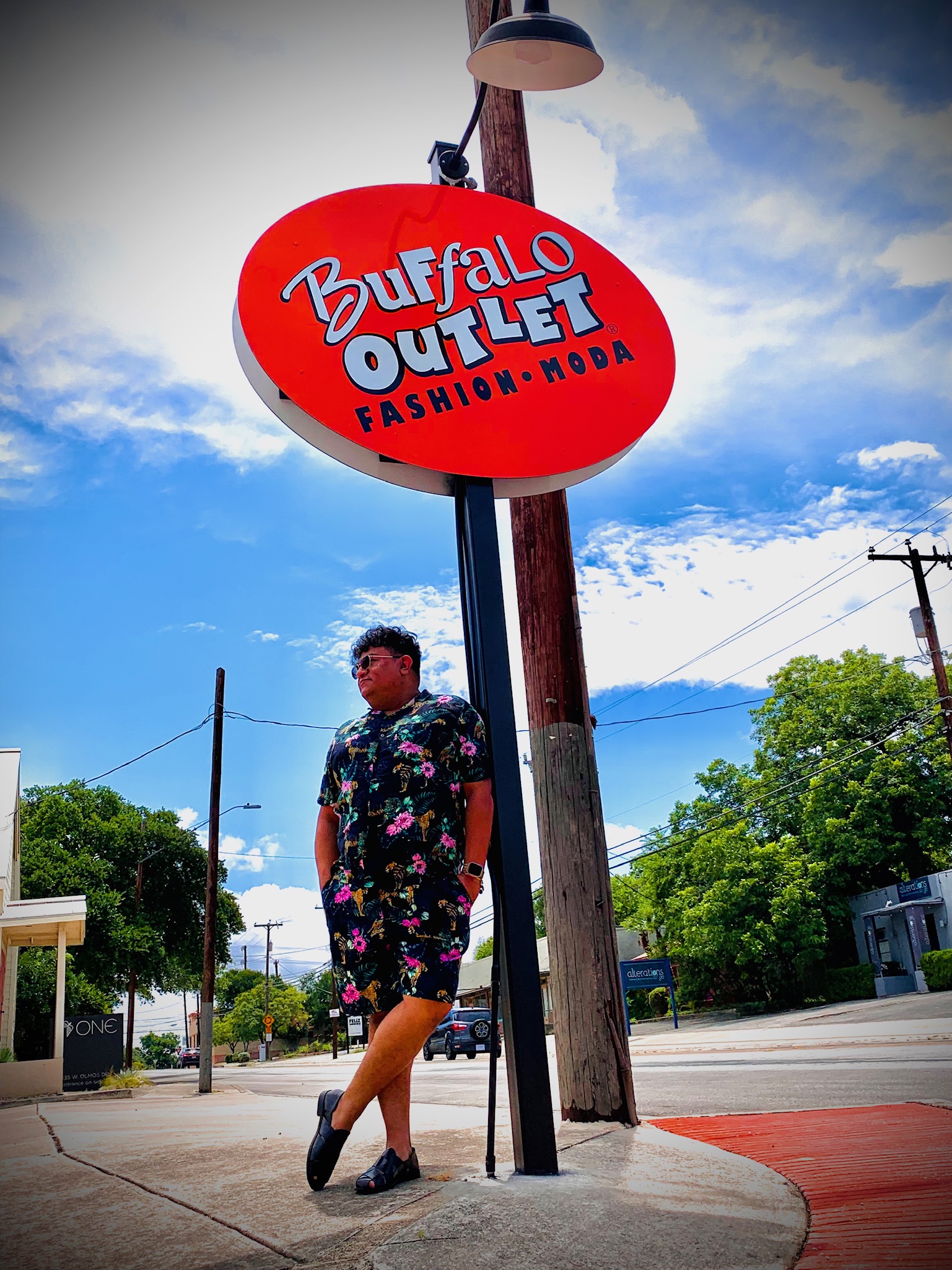 Felix wearing floral print one piece and loafers under Buffalo Outlet sign