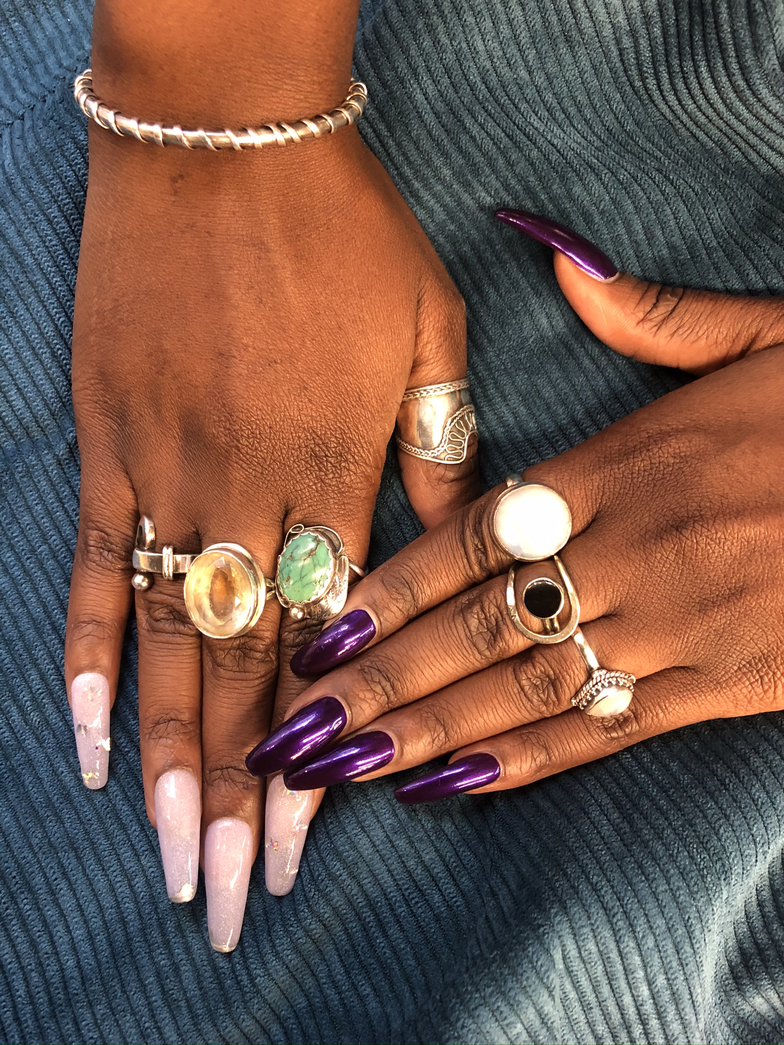 Hand with pink and purple long fake nails wearing several rings
