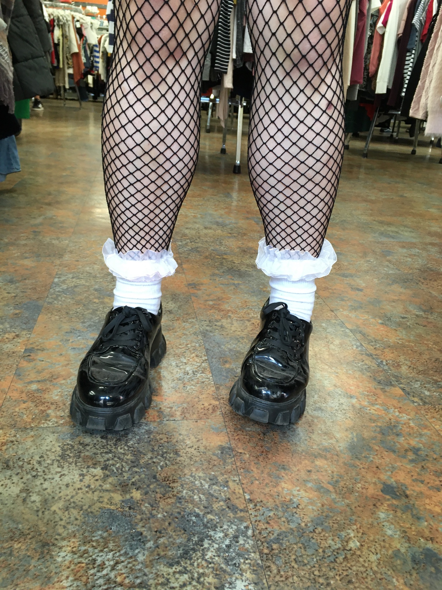 Close-up of legs with fishnet tights, white frilly sock and black platform loafers