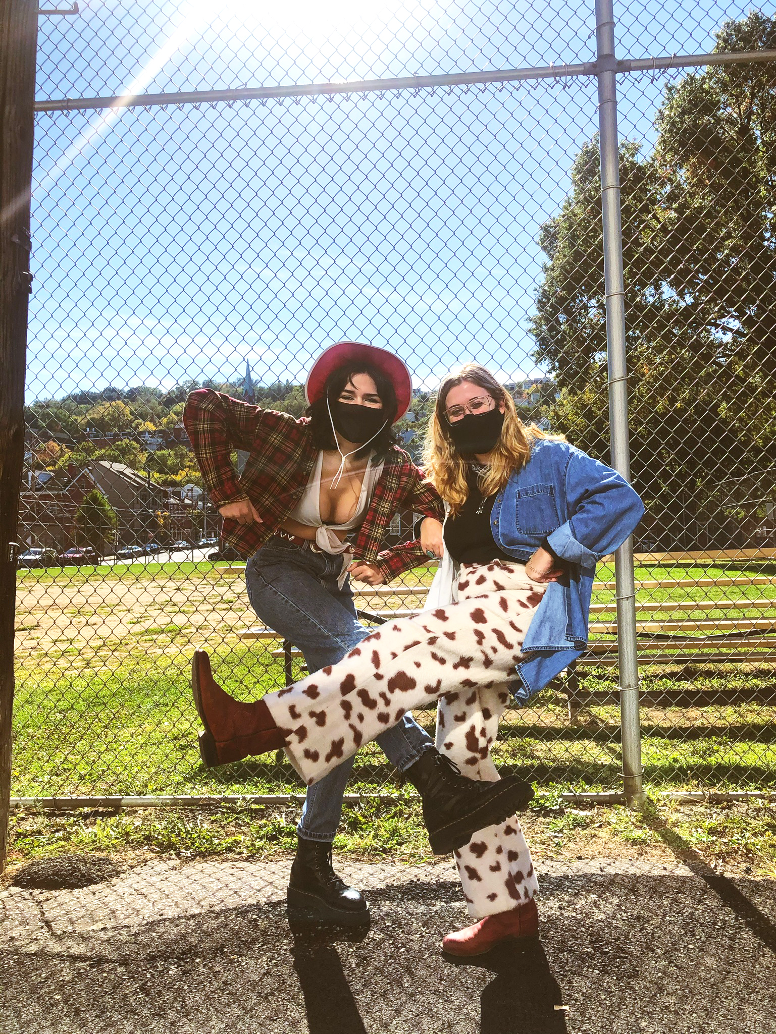 2 women standing in front of chainlink fence / baseball field wearing Western outfits