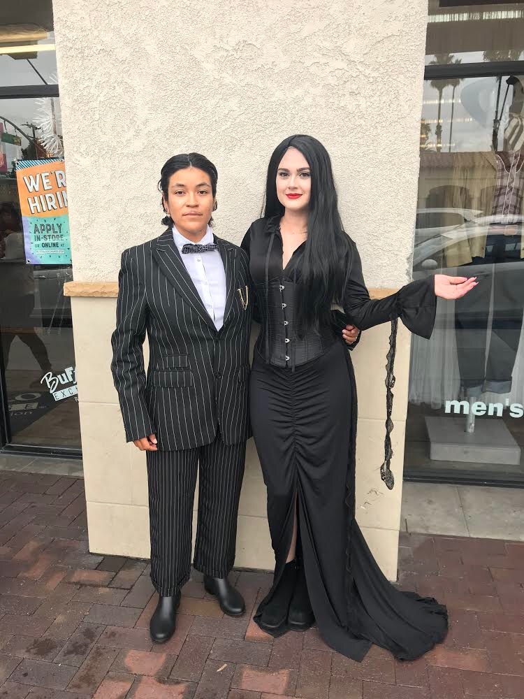 2 people dressed as Gomez in pin stripe suit and Morticia in corset and black front-slit skirt