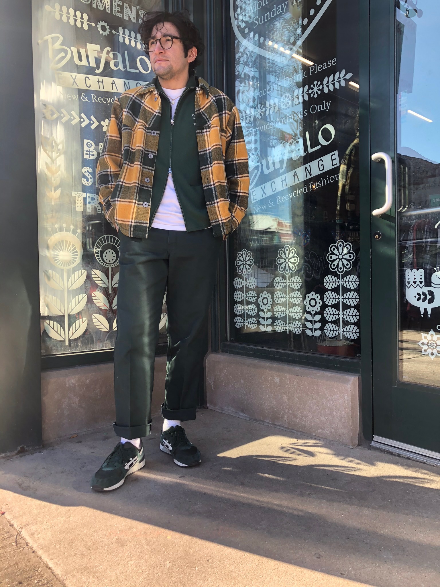 Buffalo Exchange Chicago (Andersonville) A person layering up a yellow plaid shacket over a white tee and a green jacket