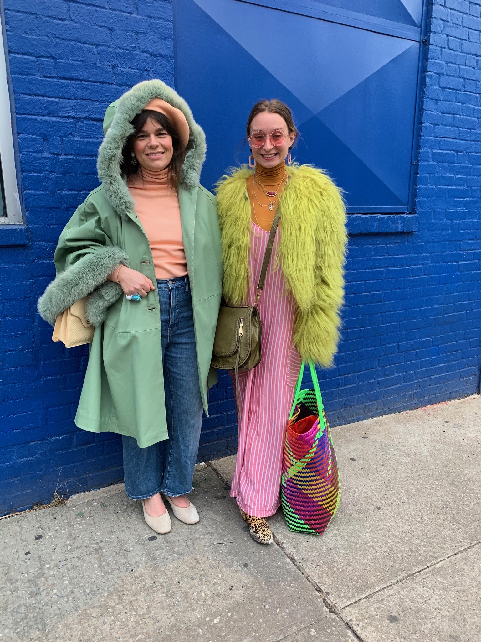 Two people standing in front of a blue wall wearing green faux fur coats