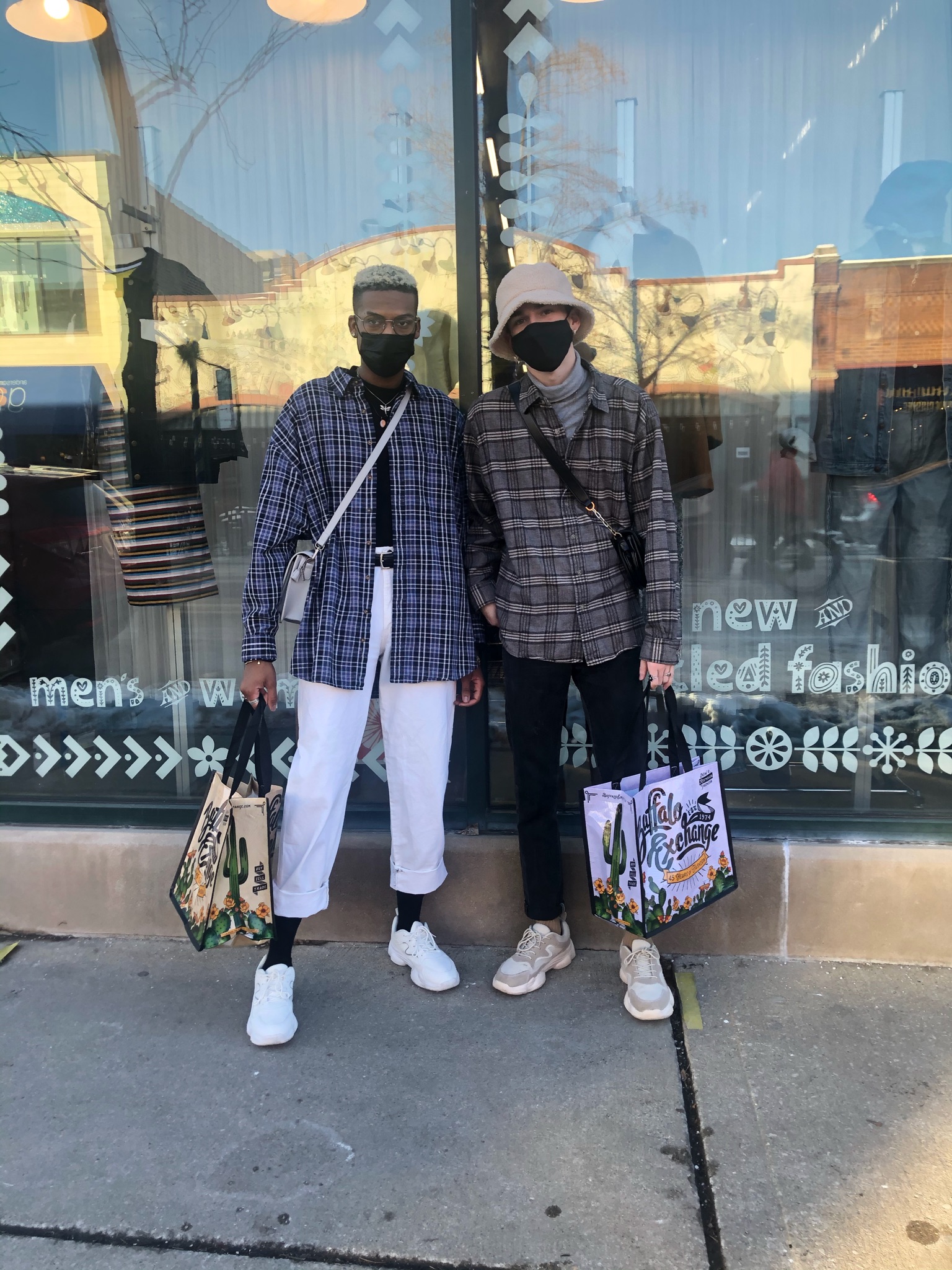 Two people wearing Plaid Shackets, cropped pants and holding a Buffalo Exchange tote