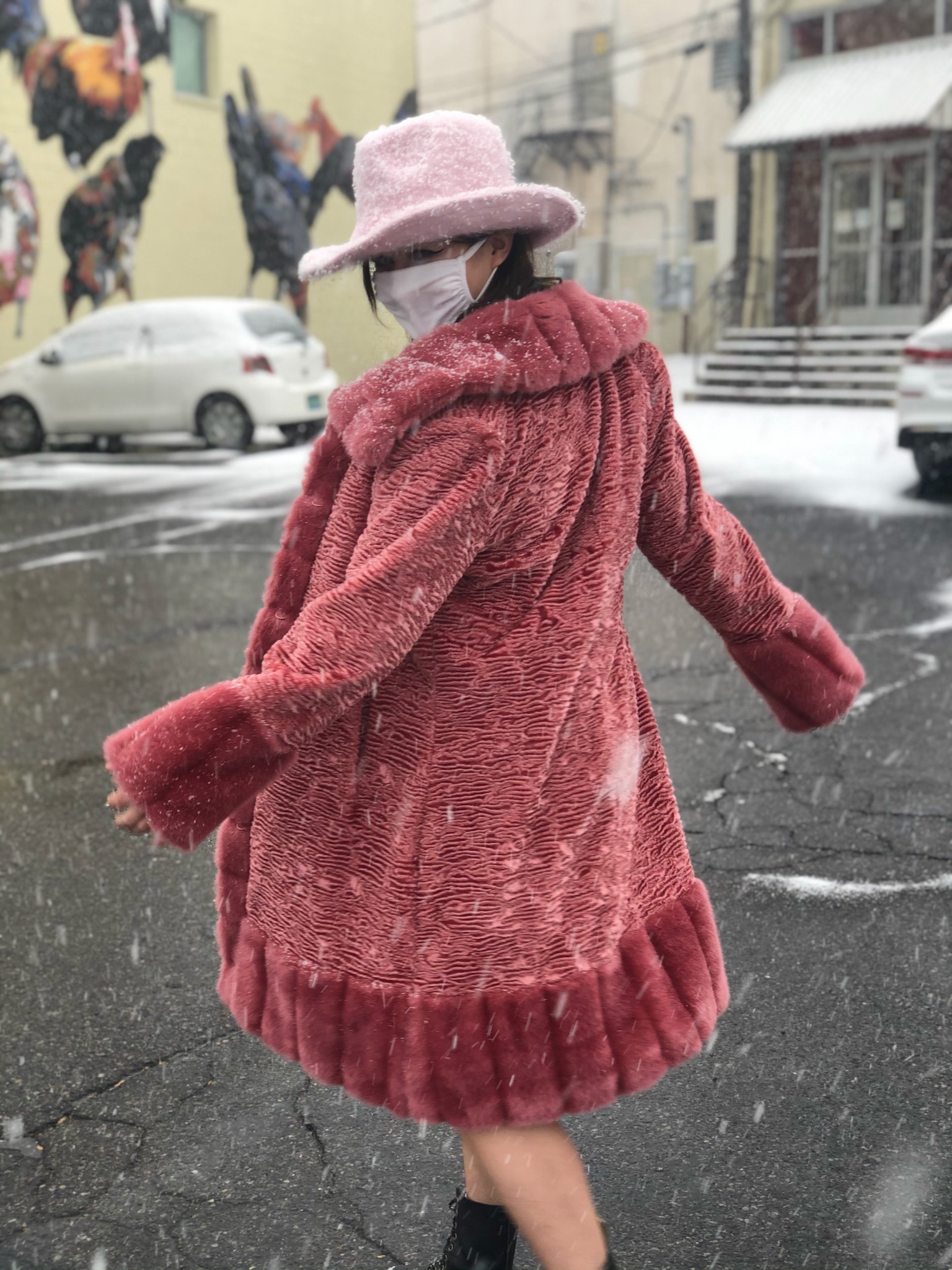 A person wearing a pink fur coat and pink fuzzy cowgirl hat in the snow