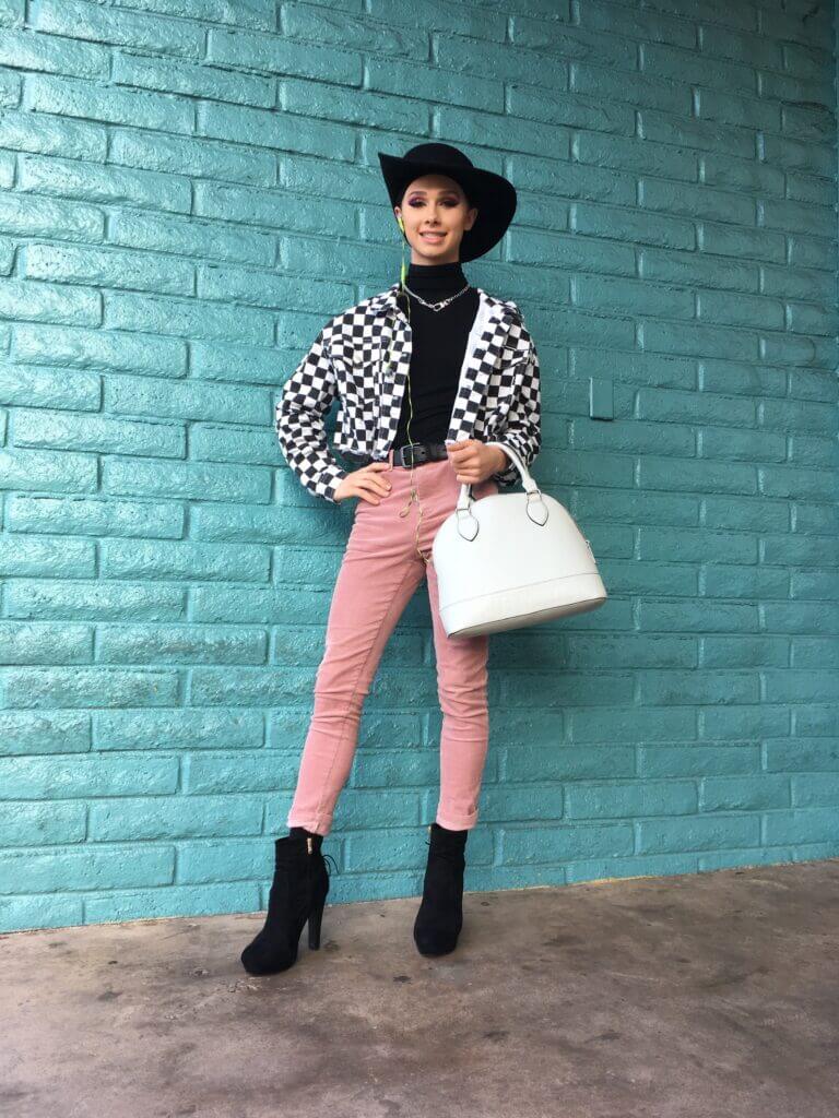 A person wearing black and white checkered jacket, pink pants, a black hat and a white handbag