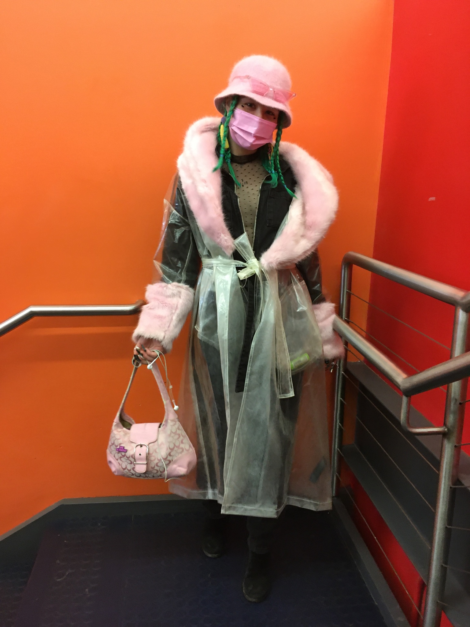 A person wearing a see through coat with pink faux fur trim and pink accessories
