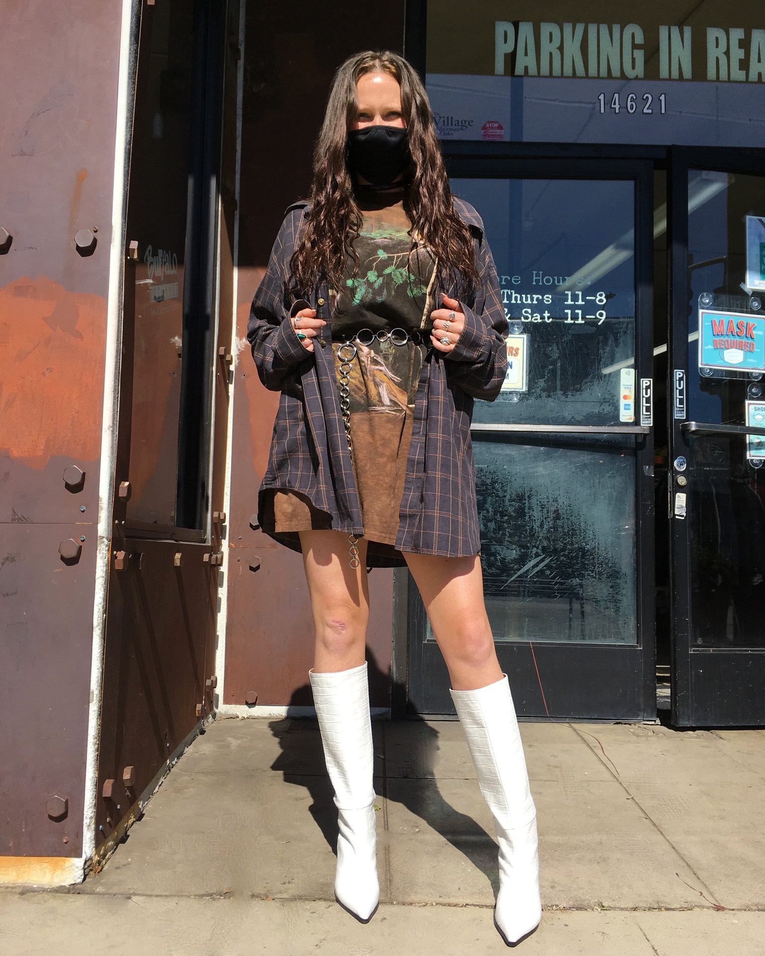 A person wearing an oversized flannel shirt over a dress and white tall boots