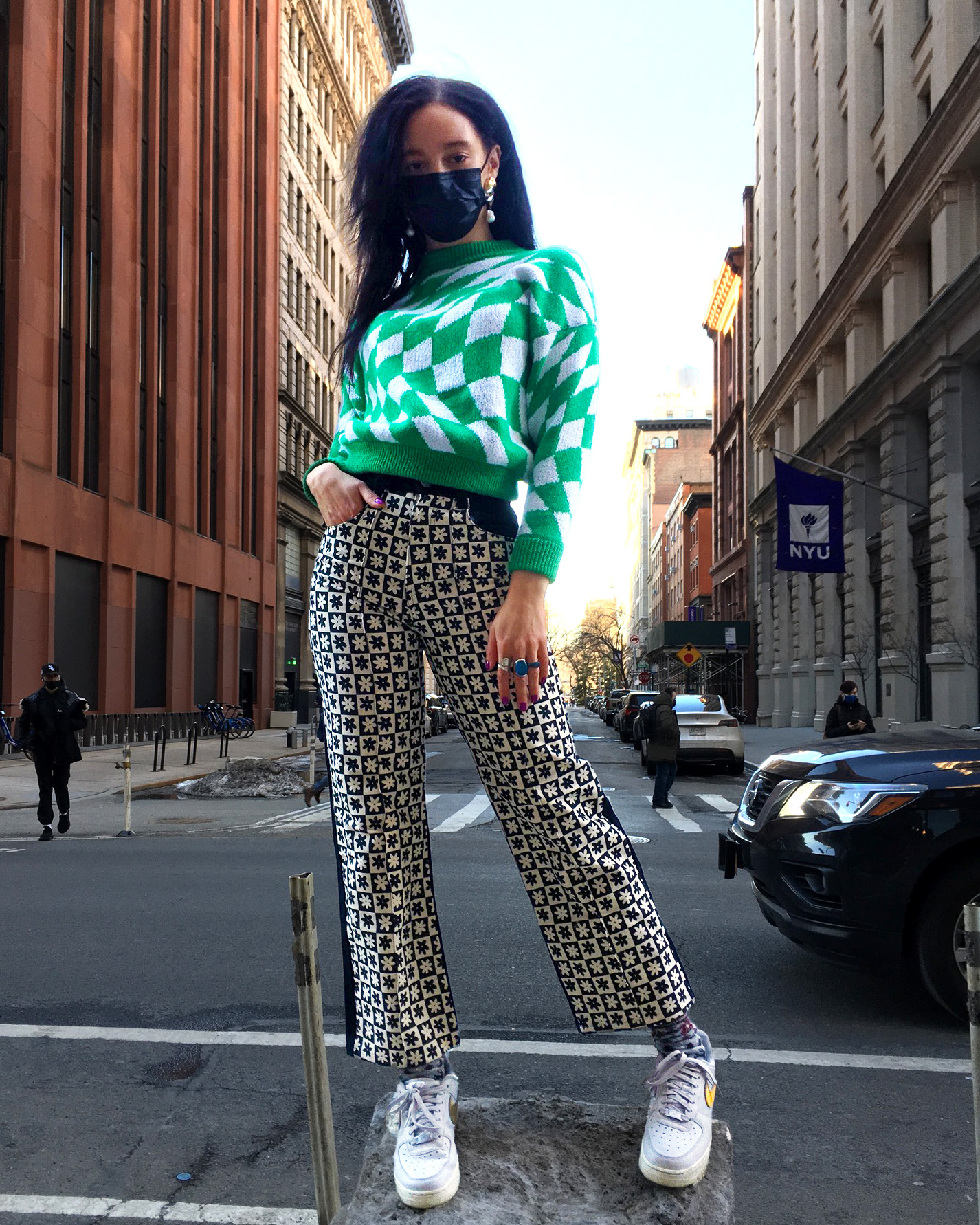 A person wearing a green and white checkered sweater and black and white geometric printed pants