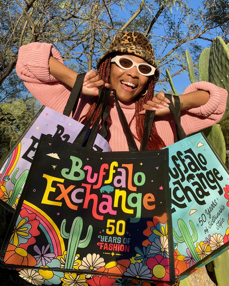 woman smiling while holding up three buffalo exchange reusable tote bags