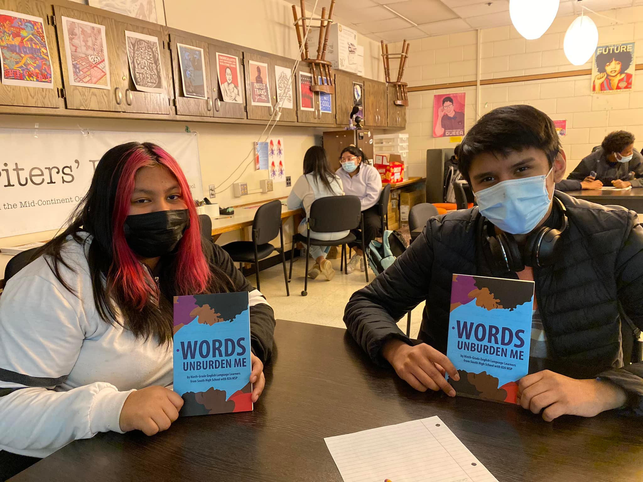 Two teenagers sitting in a classroom holding a book with the title "Words Unburden Me"