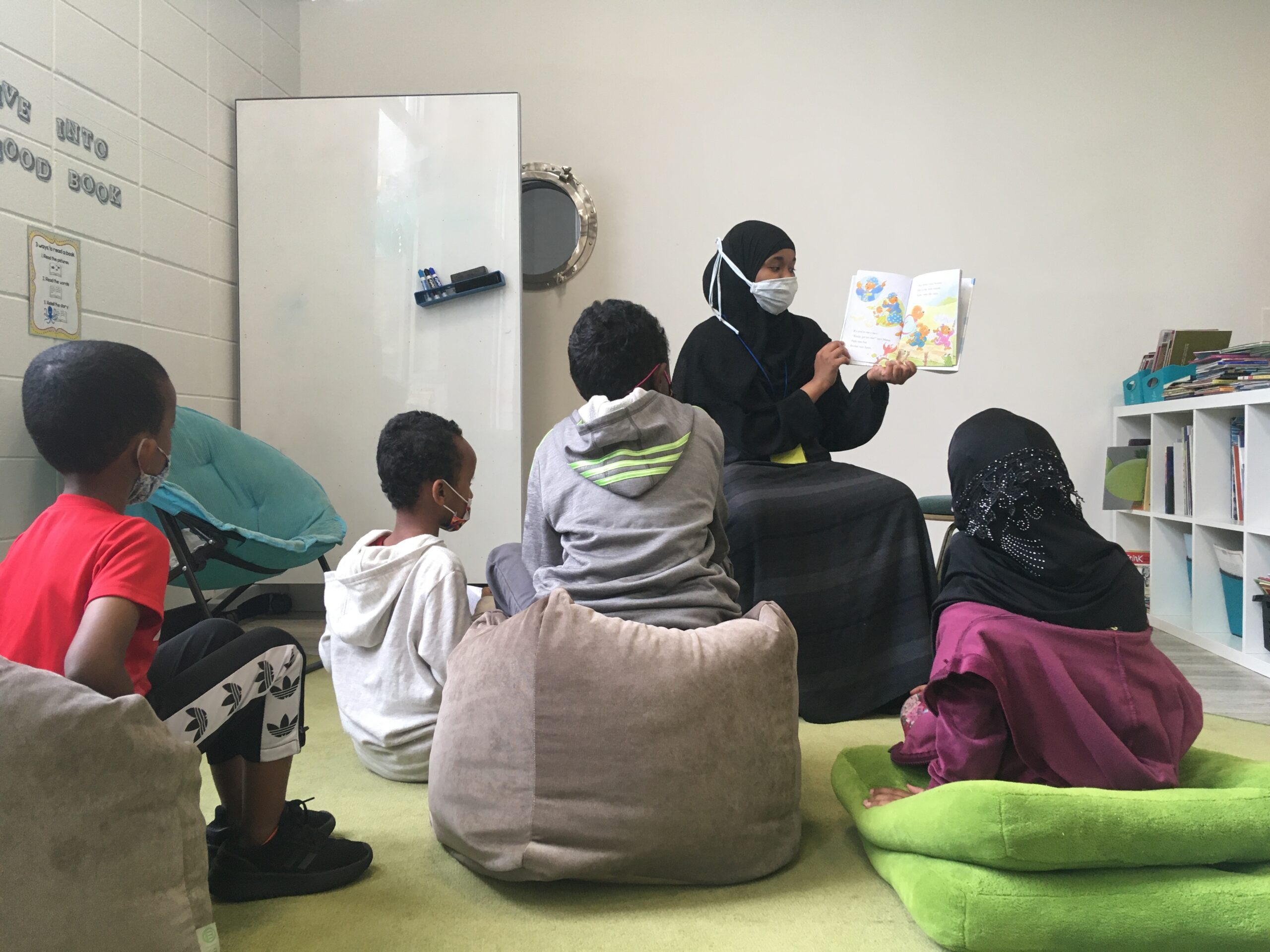 A woman reading a book to four children in a classroom