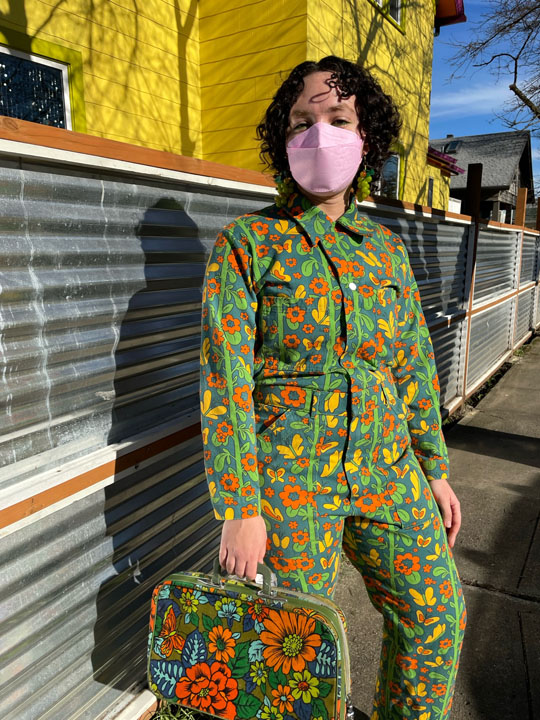 Girl posing wearing green floral jumpsuit and matching vintage luggage