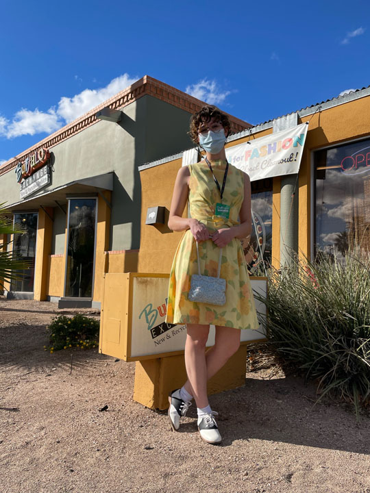 Buffalo Exchange employee posing in front of Tucson location wearing yellow floral dress