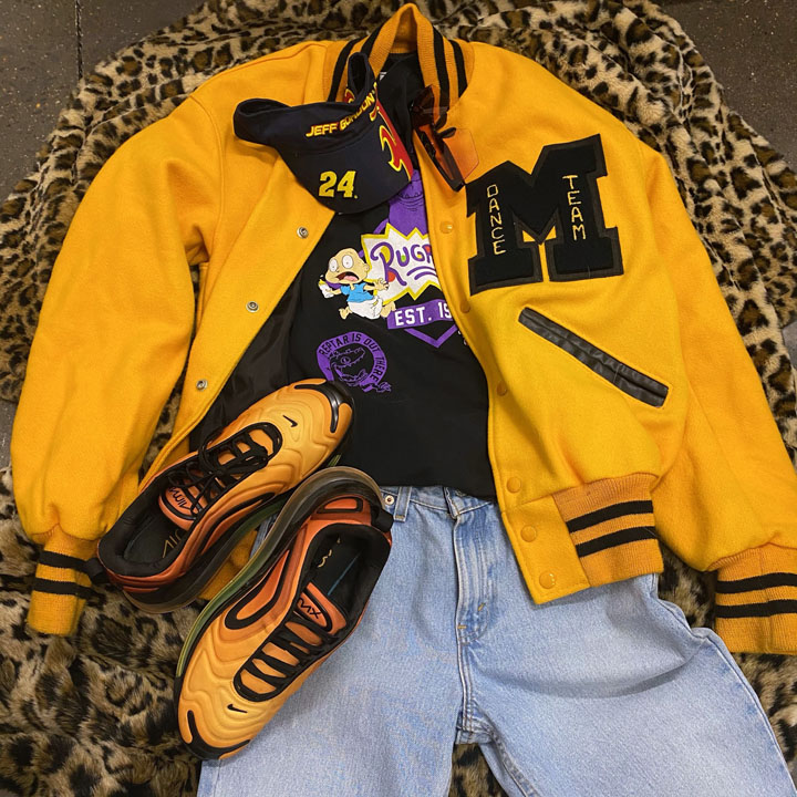 Flat lay of clothing including a Michigan varsity jacket with matching sneakers and a graphic t-shirt