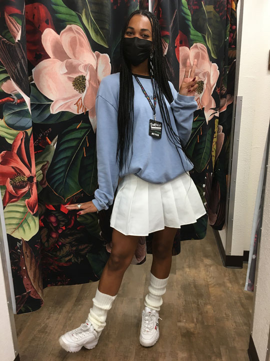 Buffalo Exchange employee posing in blue sweater and white tennis skirt