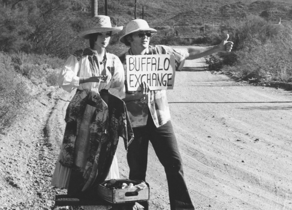 Two people hitchhiking with a sign that says buffalo exchange