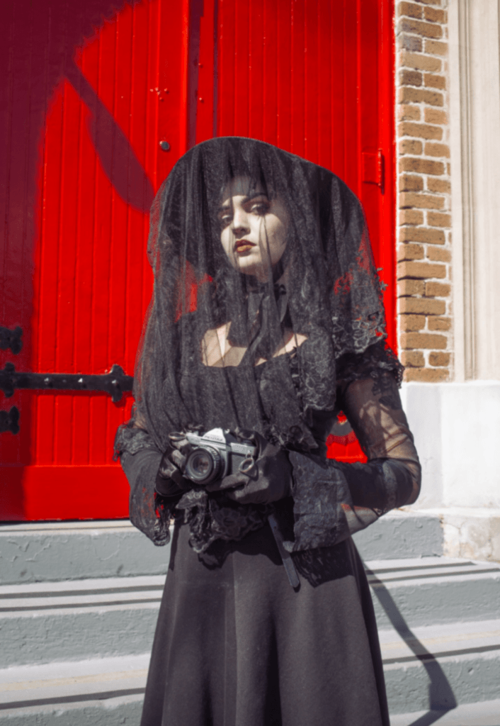 Person standing in front door wearing Lydia Deetz costume and holding old film camera