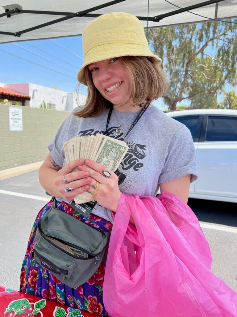 Person smiling wearing a hat and holding dollar bills outside
