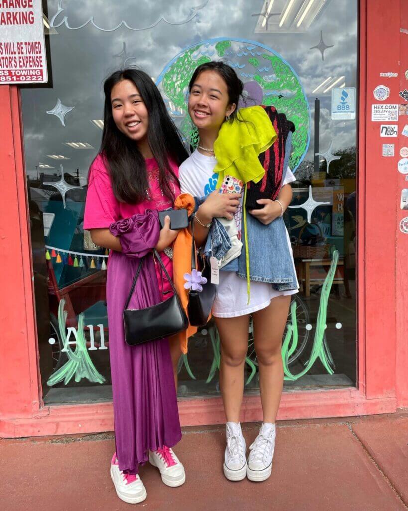 Two people smiling stand next to each other holding armfuls of clothes