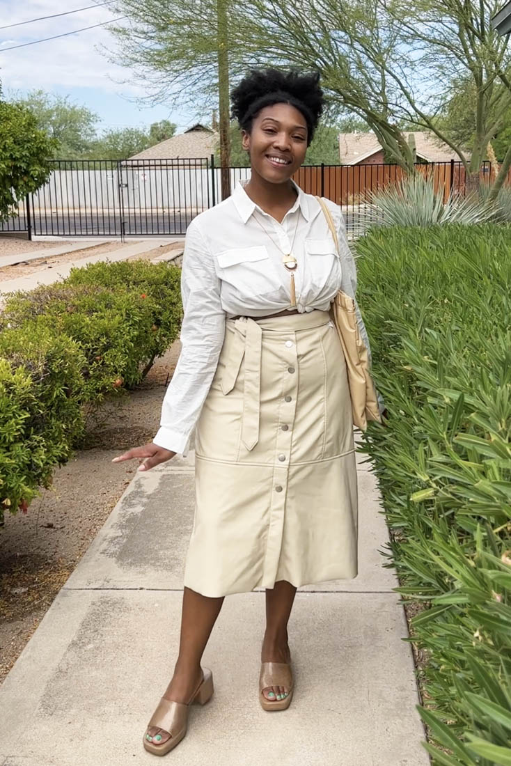 Person standing on sidewalk wearing tan midi skirt and white blouse