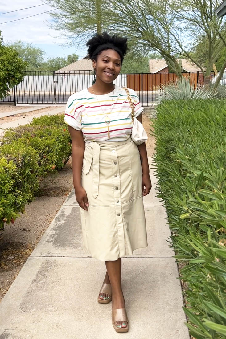 Person standing on sidewalk wearing tan midi skirt and striped t-shirt