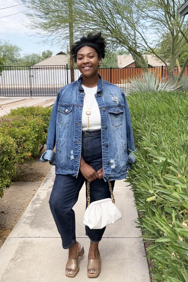 Person standing on sidewalk wearing denim jacket, white blouse and jeans