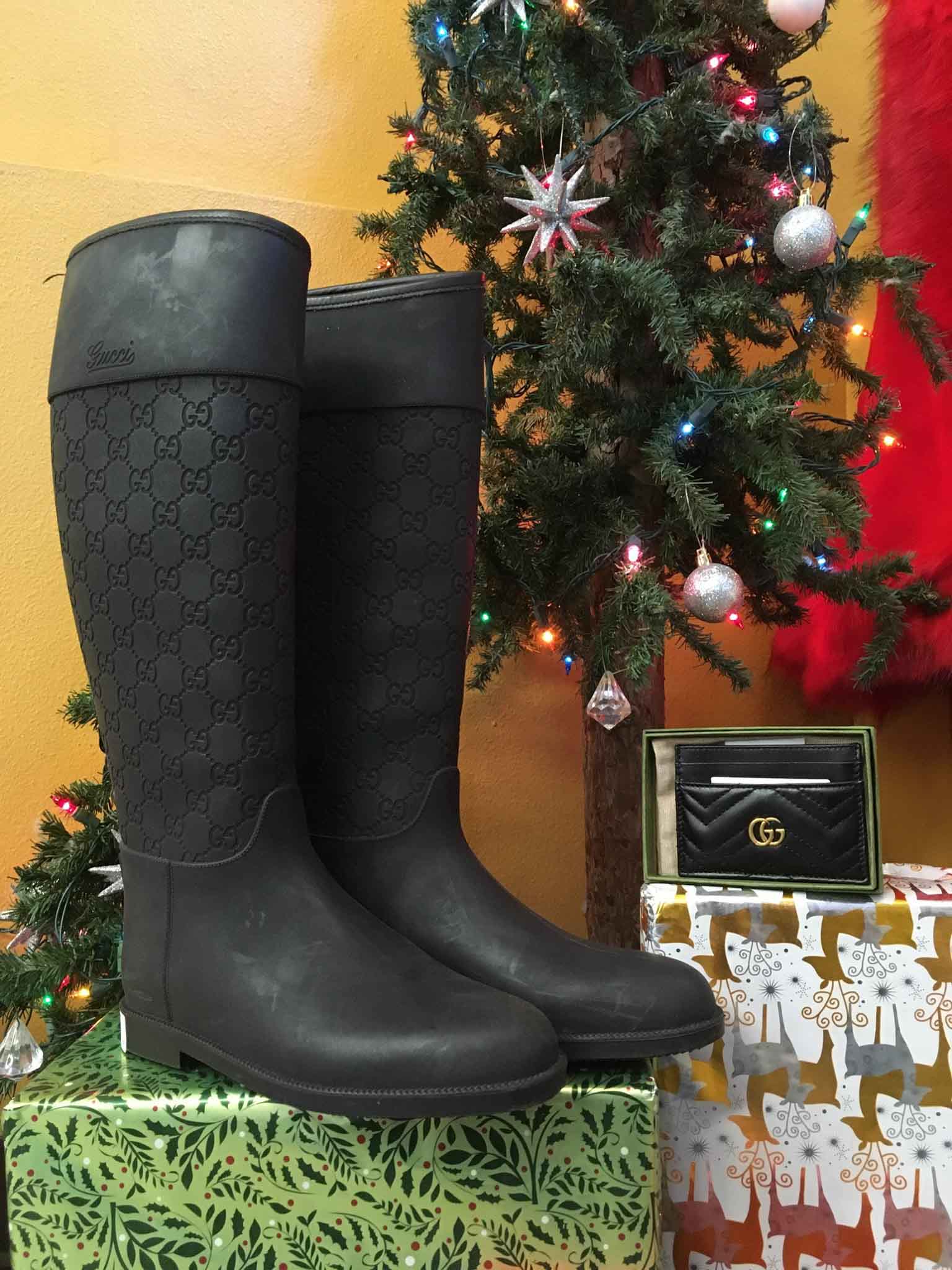 A pair of black Gucci rain boots and a Gucci card holder on top of Christmas boxes