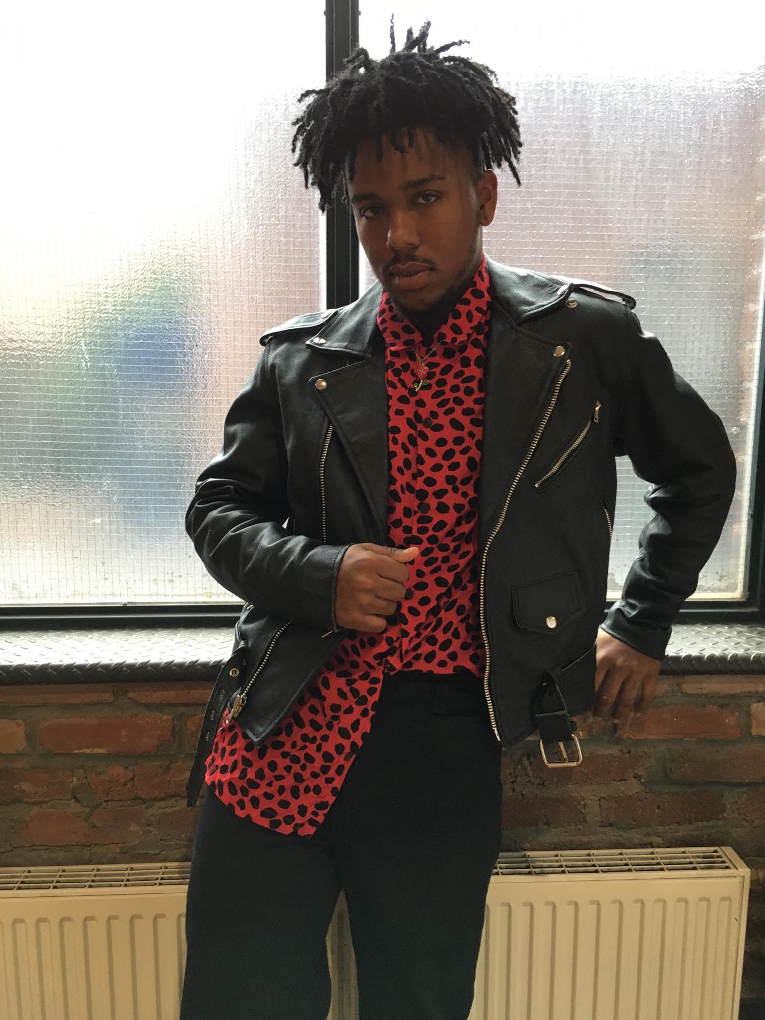 A person wearing a black leather jacket over a black and red printed shirt