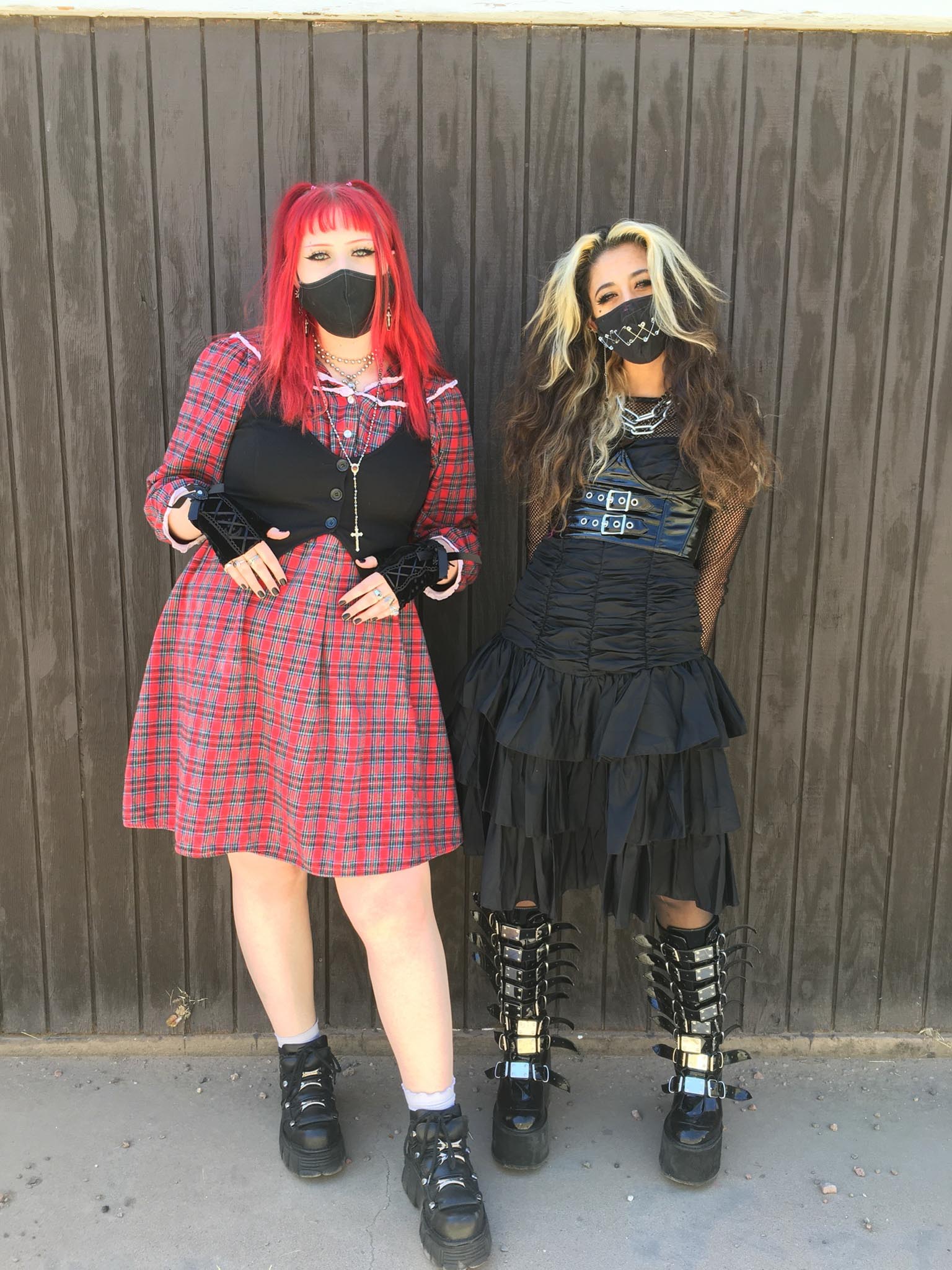 Two people wearing punk clothing, one in a red plaid dress and black vest, the other in a black dress with leather corset and silver-buckled boots.