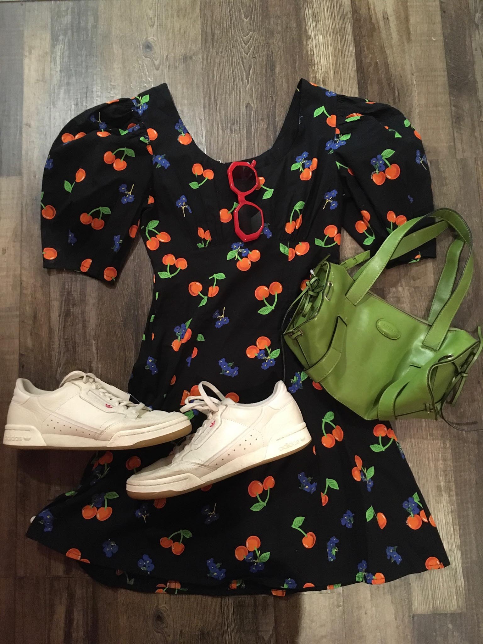 black cherry print dress, red framed sunglasses, green handbag and white Reebok sneakers