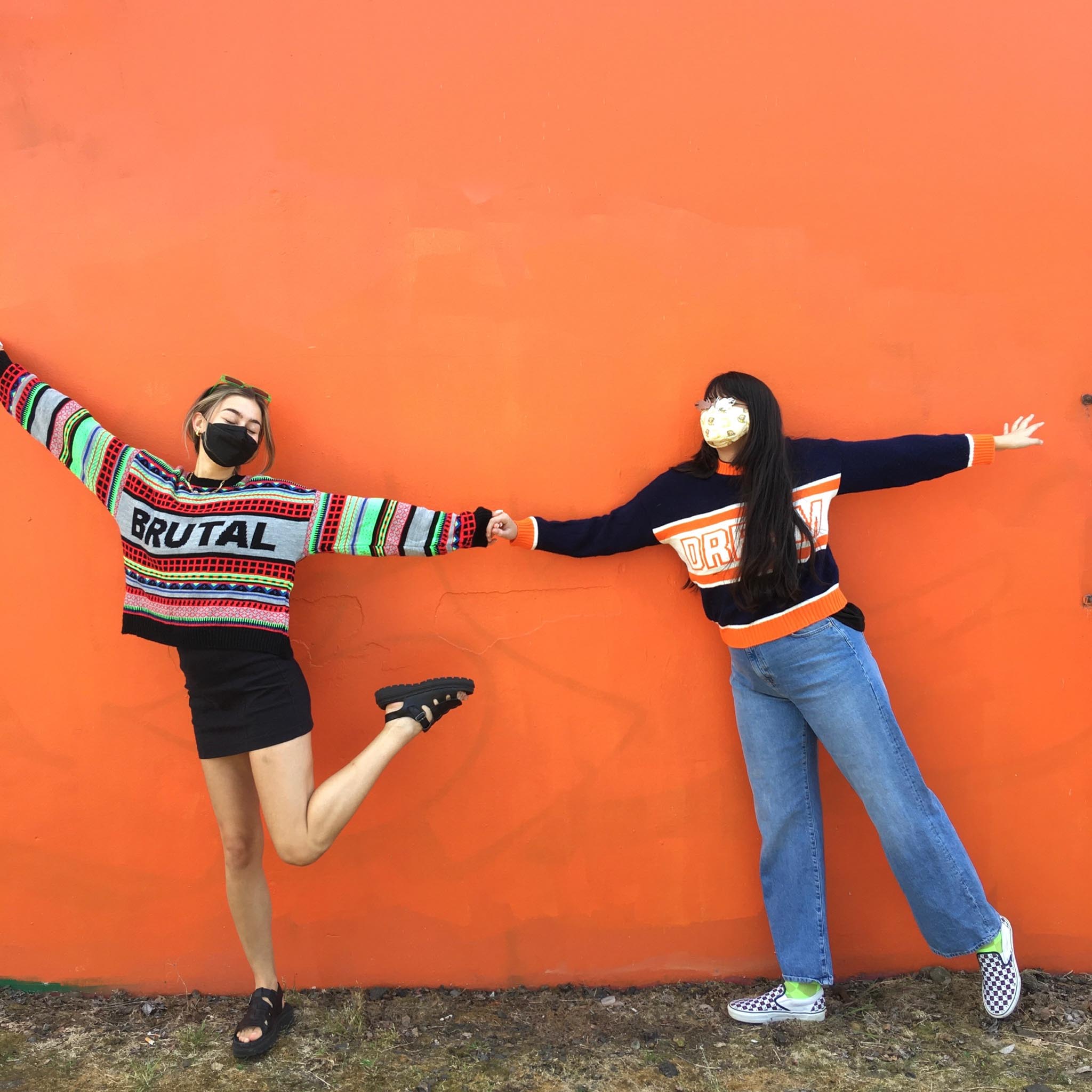 Two people posed holding hands wearing sweaters with intarsia stitching that reads "BRUTAL" and "DREAM"