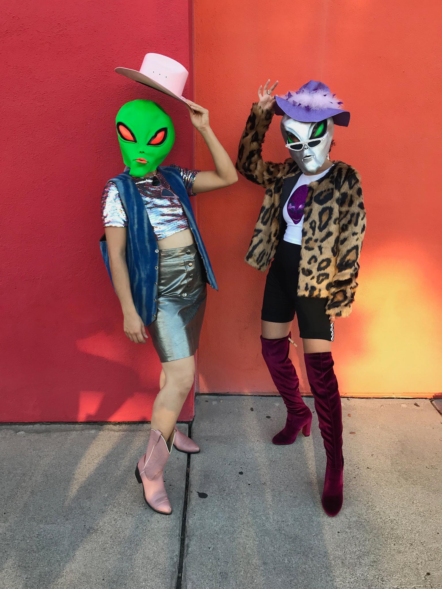 2 People in front of red and orange wall dressed as space cowgirls & wearing alien masks