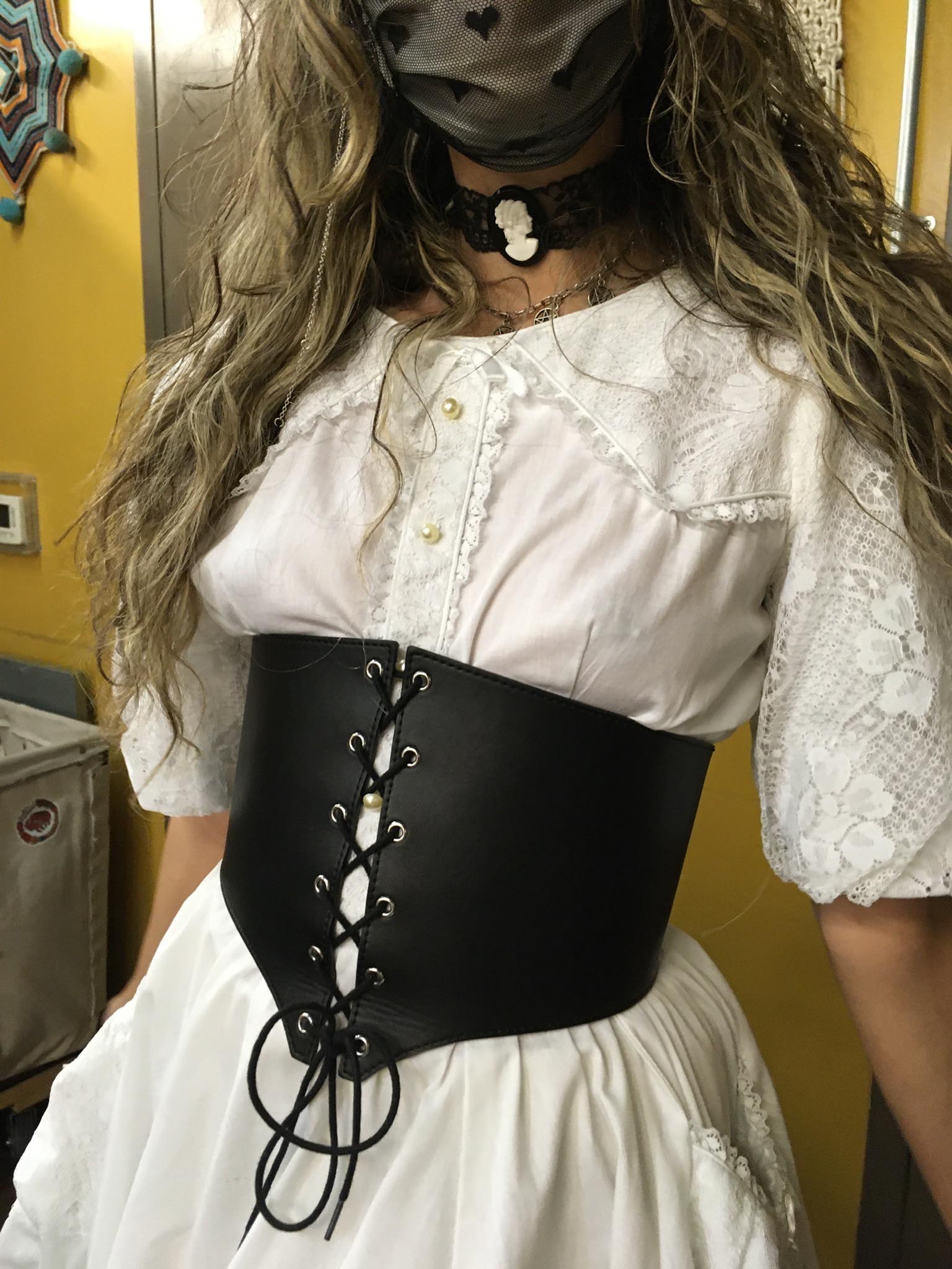 Person wearing black corset belt over white, Victorian-inspired dress