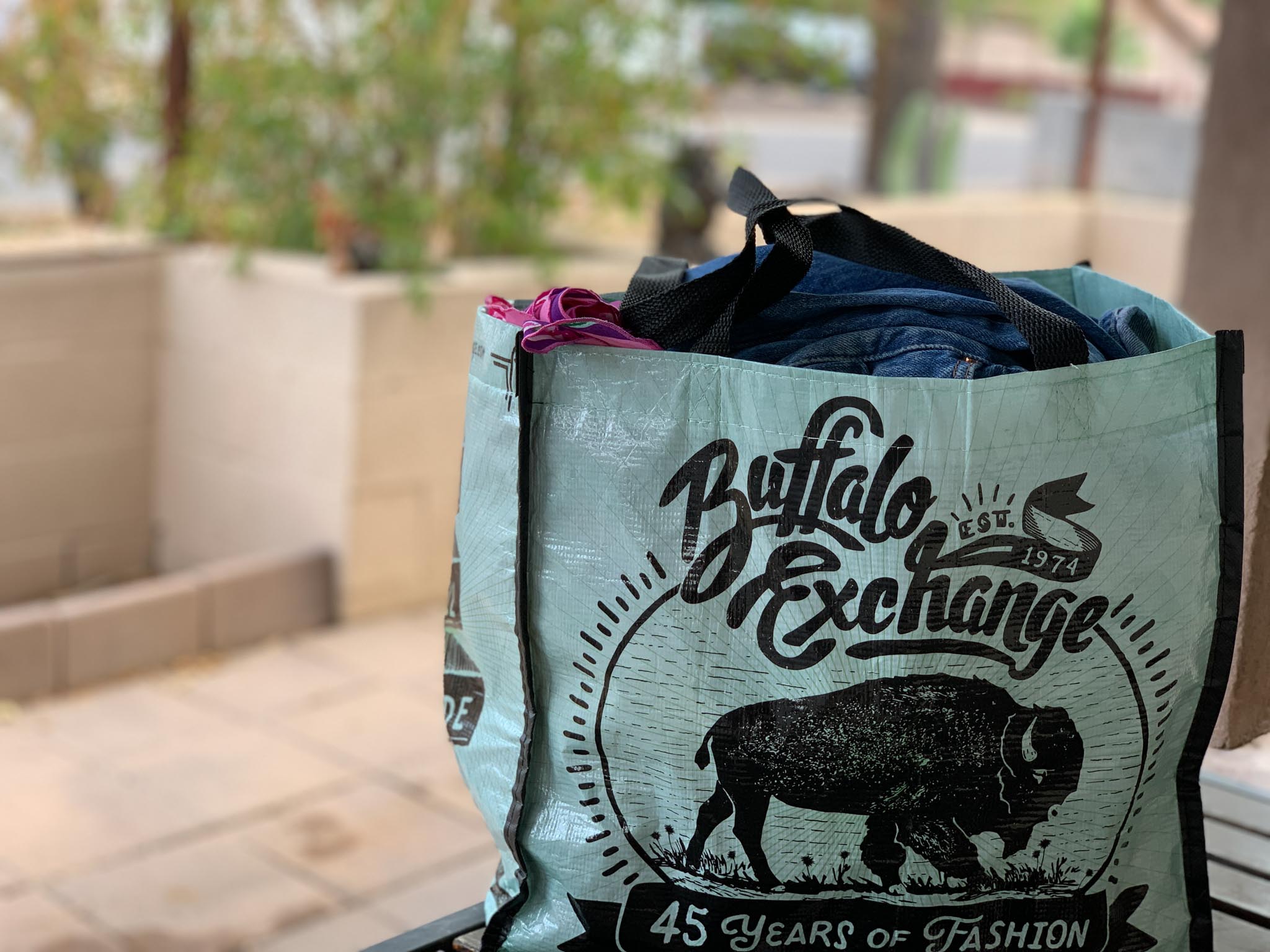 A light blue Buffalo Exchange reusable plastic tote bag filled with clothes ready to sell