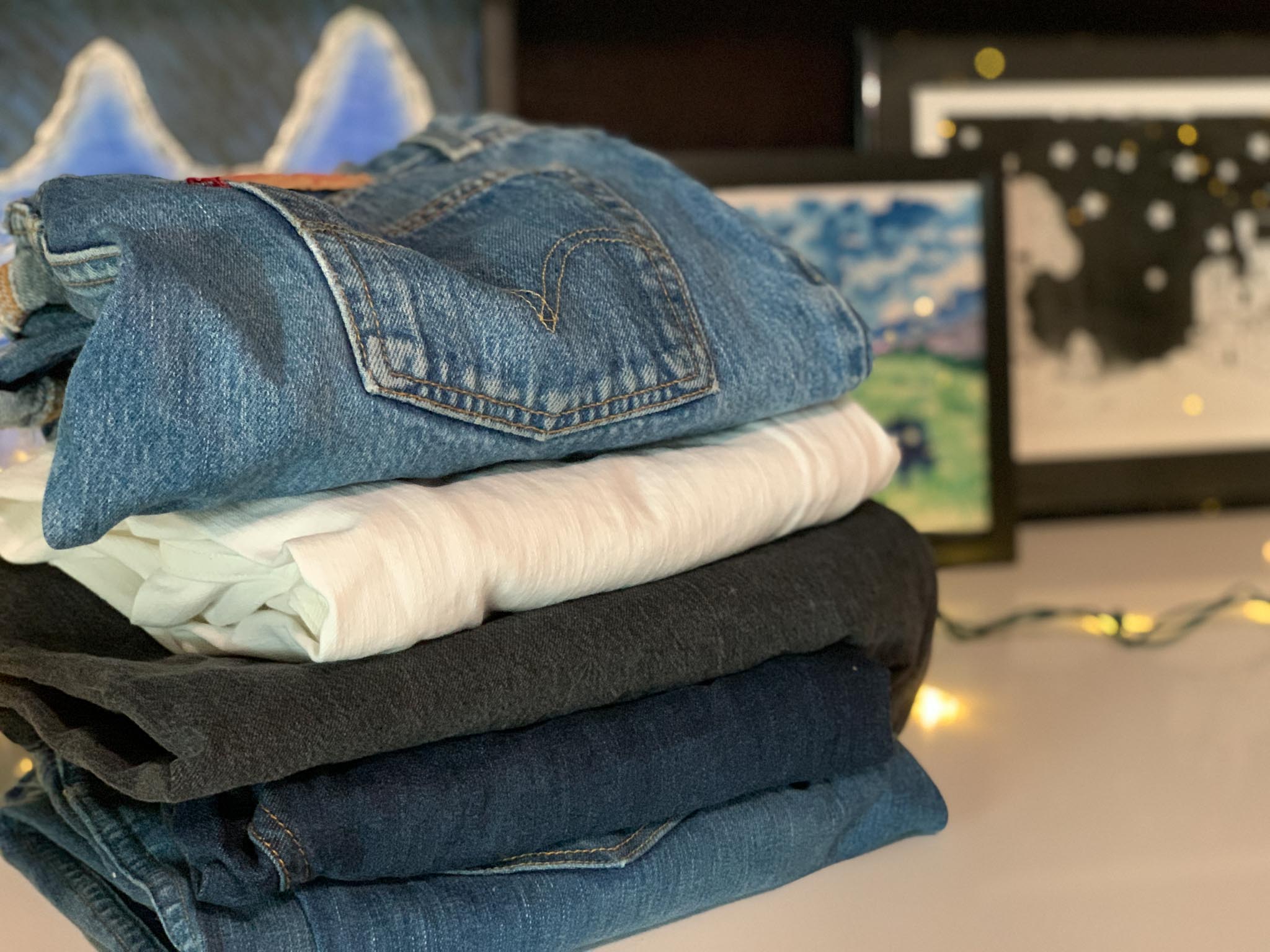Things I Think About When I Sell My Clothing - Photo of 5 pairs of jeans in a stack with artwork in the background