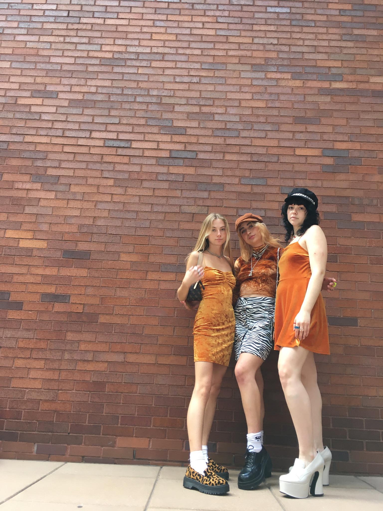 Three women standing outside in front of red brick wall wearing orange velvet