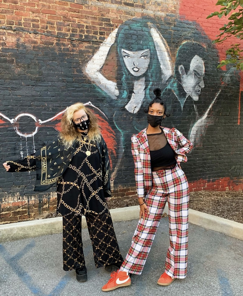 Two people dressed in matching sets of chain-print and plaid standing in front of a mural