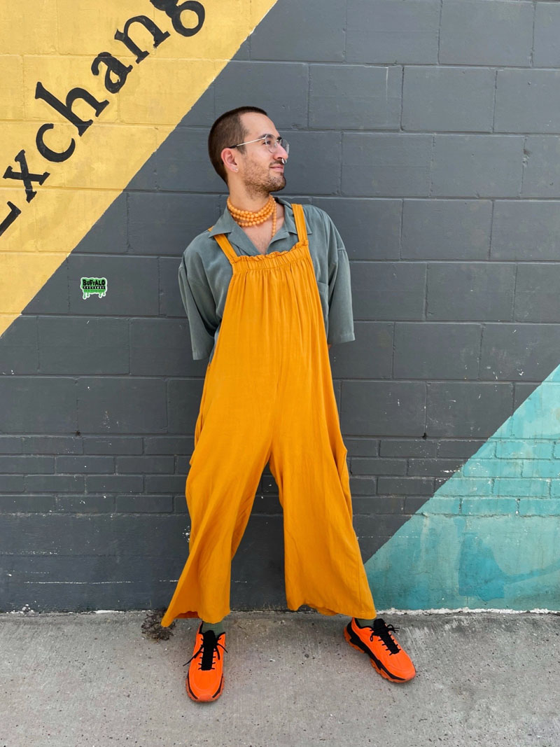 Person standing in front of striped mural wearing a mustard yellow jumpsuit 